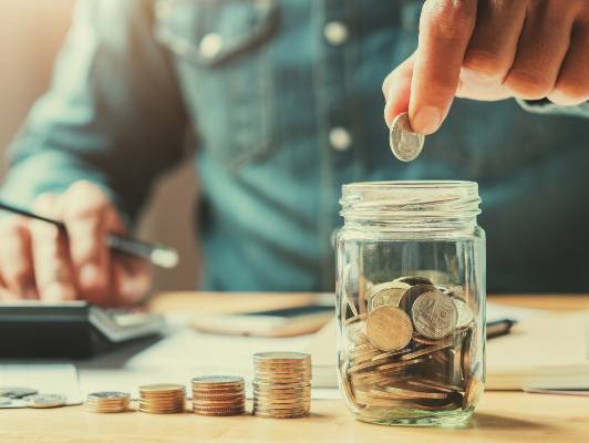 Geschäftsmann lässt Münzen ins Glas fallen. Konzept Geld zu sparen.